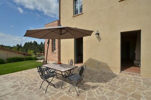 An outdoor patio with a table and chairs, a large umbrella, and a brick wall. - Apartment Pino - 2 Bedroom Apartment in Tuscany (Trequanda)