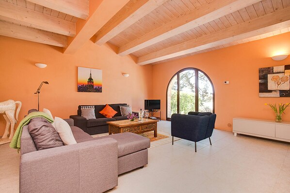 A living room with a sofa, armchair, coffee table, and a TV. There is a painting on the wall and a window with a view of greenery. - Villa Pesca Amazing House in the Heart of Tuscany (Trequanda)