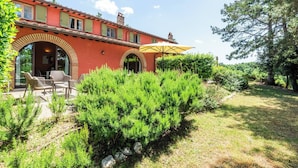 Eine rote Villa mit Terrasse, Sitzgelegenheiten im Freien und einem gelben Sonnenschirm.