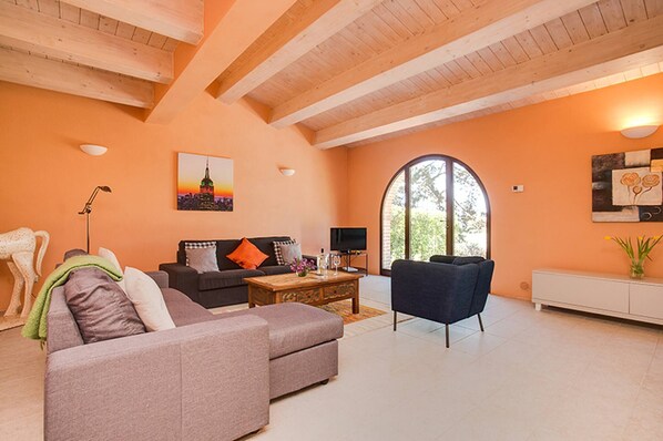 A living room with a sofa, armchair, coffee table, and a TV. There is a painting on the wall and a window with a view of greenery. - Villa Pesca Amazing House in the Heart of Tuscany (Trequanda)