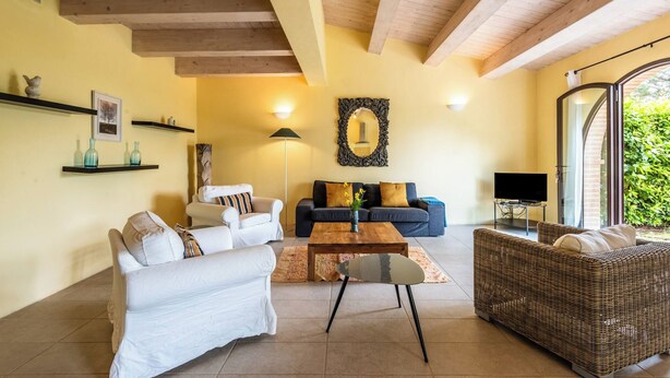 A living room with a sofa, a coffee table, and a wicker sofa. There is a TV on a stand and a window with a view of greenery. - Villa Limone - 3 Bedroom Villa in Tuscany (Trequanda)
