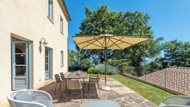 Een terras buiten met een tafel, stoelen, een grote parasol en een stenen muur.