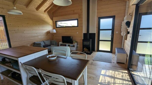 Ein Holzhäuschen im Inneren mit Esstisch, Stühlen, einer Couch, einem Fernseher und einem Kamin.