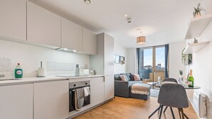 A modern kitchen with white cabinets, a built-in oven, and a dining area with a grey sofa and a small table. - Apt-sleeps 2/3-bullring & Grand Central Close (Birmingham)