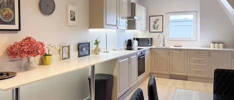 Una cocina moderna con encimera blanca, electrodomésticos de acero inoxidable y un cubo de basura negro.
