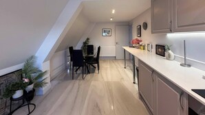 A modern kitchen with a dining area, featuring a long countertop, cabinets, and a dining table with chairs. - Contemporary 2 Bed Apt in Didcot (Sleeps 7) (Didcot)