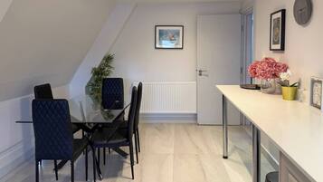 Een moderne keuken met een wit aanrecht, zwarte stoelen en een potplant.