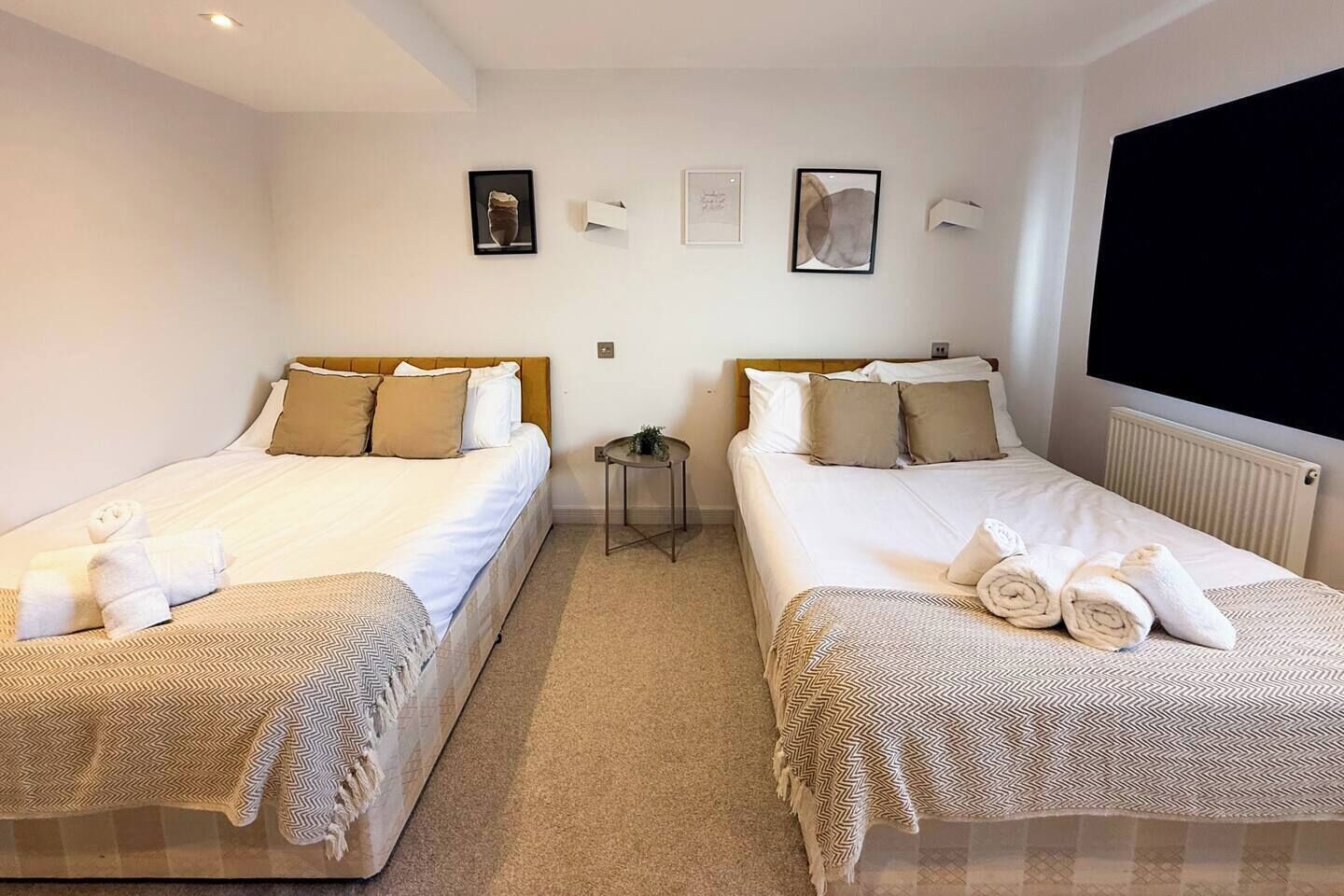 A hotel room with two beds, each with a patterned bedspread and pillows, a small side table, and a wall-mounted TV.