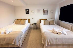 Habitación de hotel con dos camas, cada una con una colcha y almohadas estampadas, una mesita auxiliar y un televisor montado en la pared.