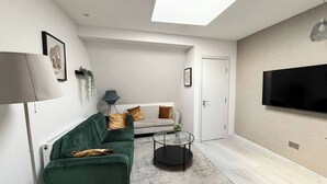 A modern living room with a green sofa, a grey sofa, a round coffee table, a floor lamp, a flat-screen TV, and a skylight. - Contemporary 2 Bed Apt in Didcot (Sleeps 7) (Didcot)