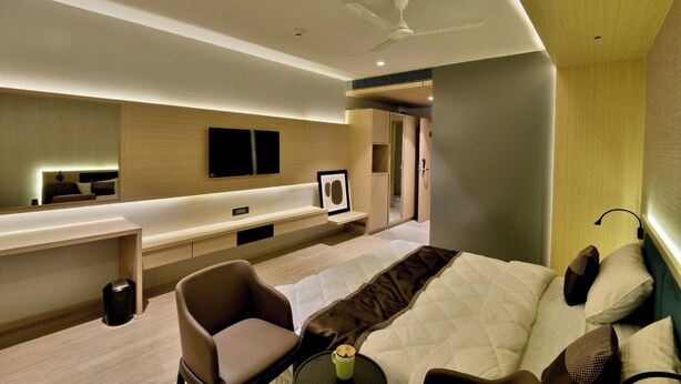 A modern hotel room with a bed, a desk, a chair, a TV, and a wardrobe. - Kratos Club (Surat)