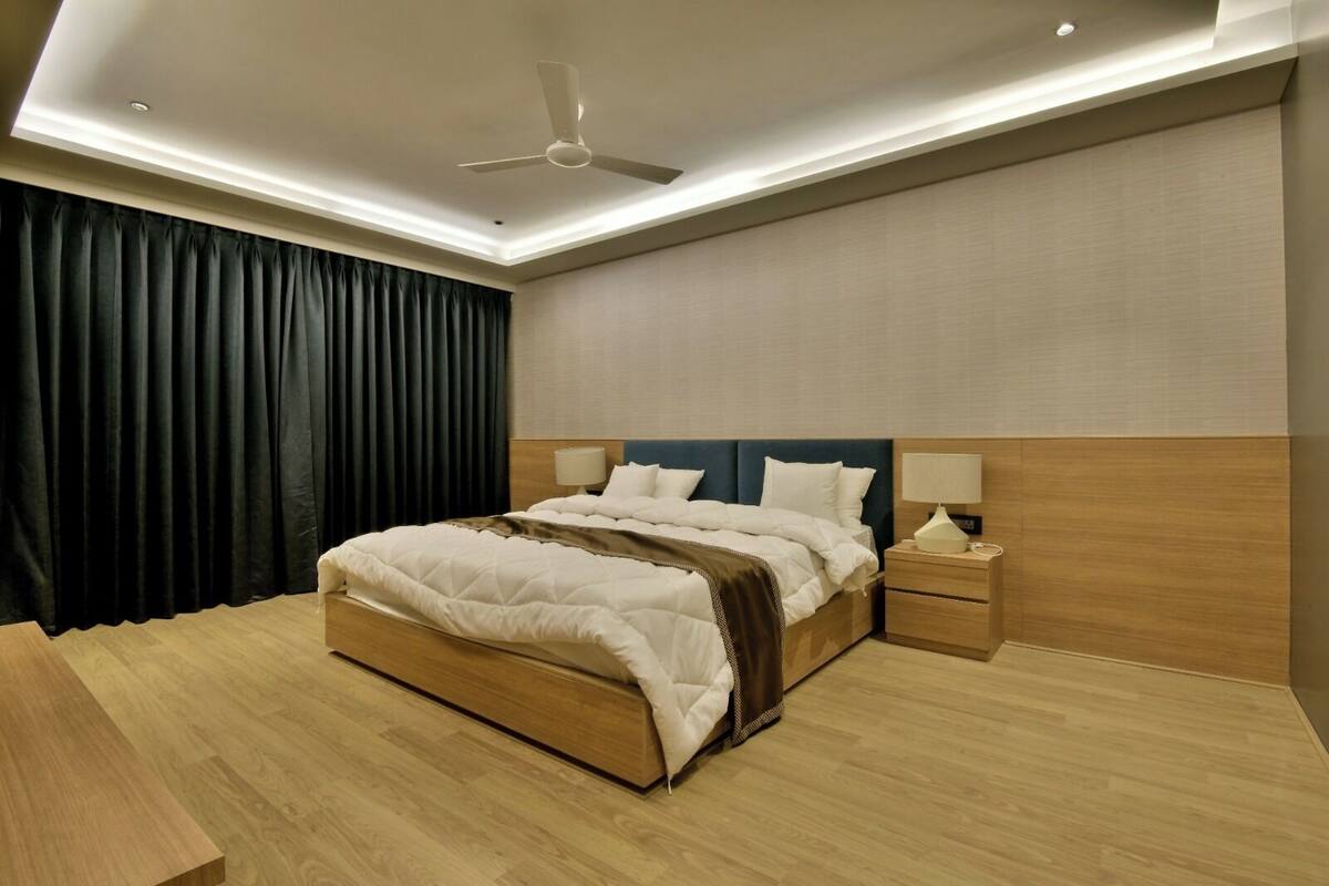 Un dormitorio de hotel moderno con una cama grande, cabecera de madera, lámparas de noche y ventilador de techo.
