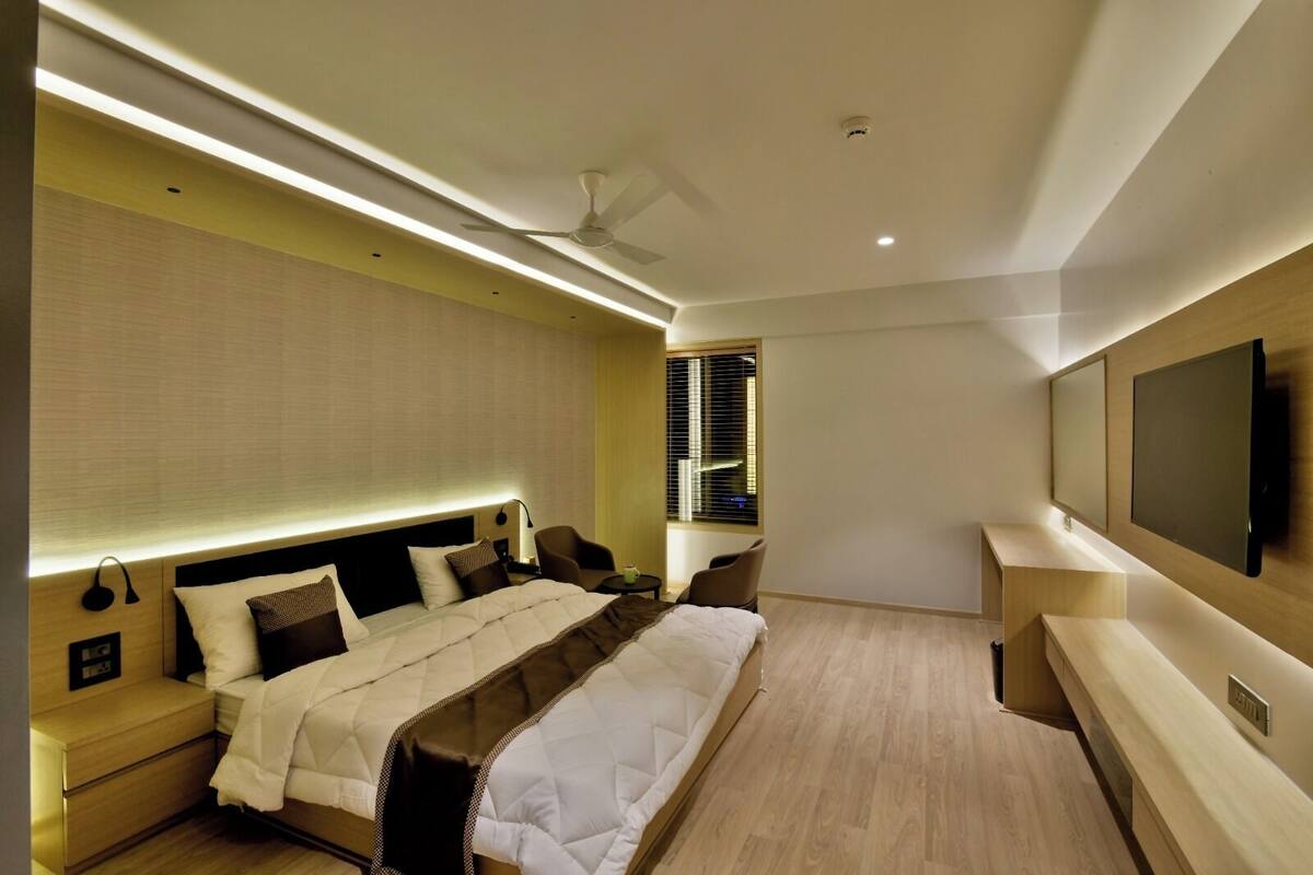 Una habitación de hotel moderna con una cama grande, mesitas de noche, televisión y ventana con persianas.