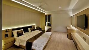A modern hotel room with a large bed, bedside tables, a TV, and a window with blinds. - Kratos Club (Surat)