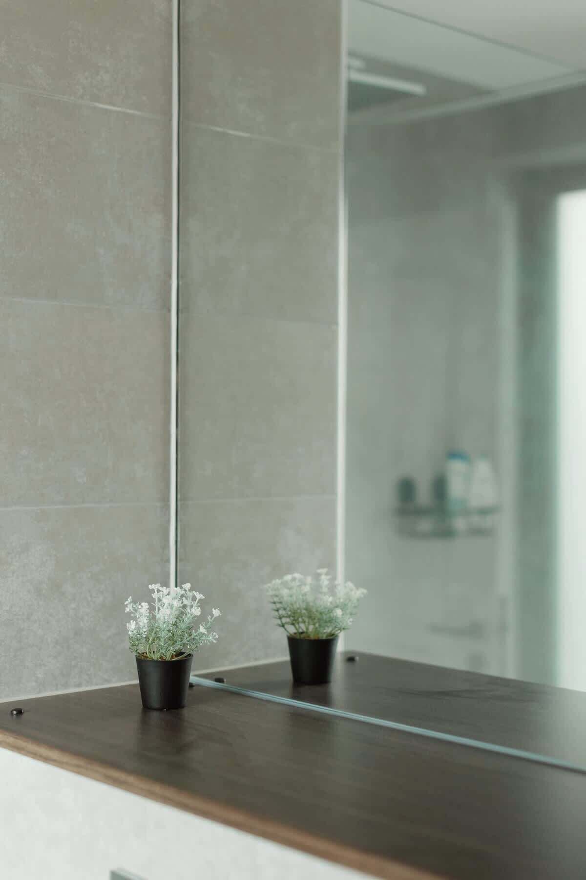 A bathroom with a large mirror, two potted plants on a wooden counter, and a tiled wall.