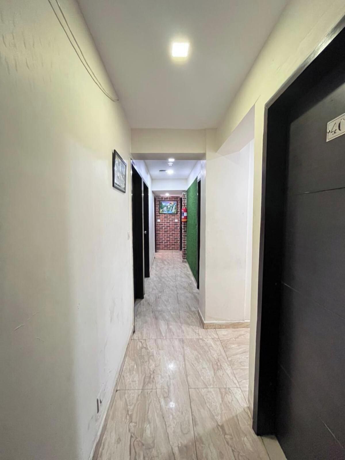 Um corredor com piso de azulejos, um quadro na parede esquerda e uma porta com uma placa à direita.