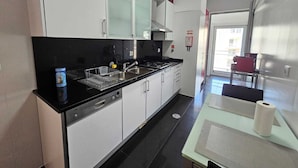 Cozinha moderna com armários brancos, bancada preta e pia de aço inoxidável. Há um escorredor de louça, uma lata de comida e um rolo de papel toalha na bancada.