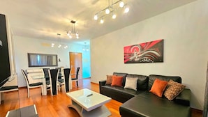 Uma sala de estar moderna com um sofá de couro preto, uma mesa de centro de vidro e uma área de jantar com uma mesa e cadeiras brancas.