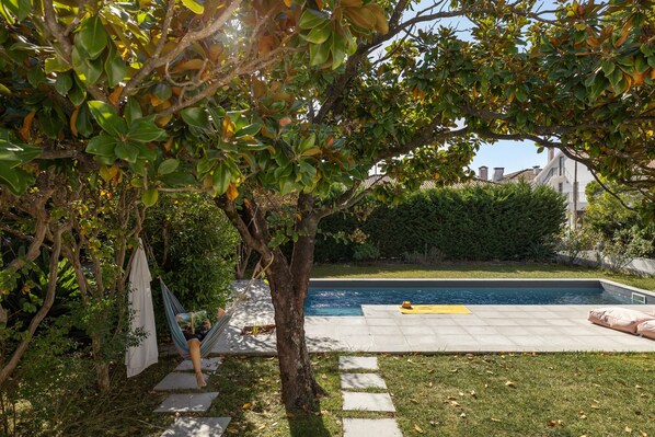 A swimming pool with a tiled deck, surrounded by greenery and a hammock. - Casa dos Limões - Oeste (Bombarral)