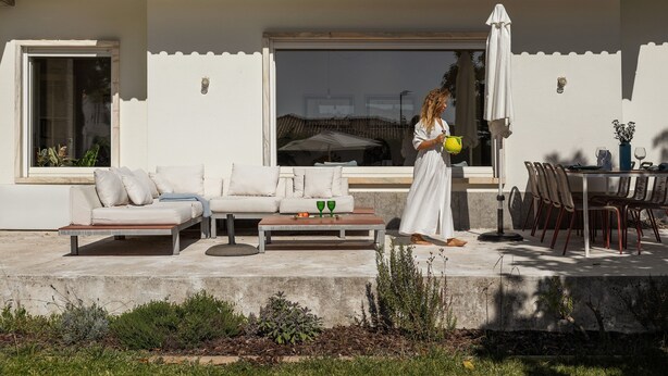 A modern outdoor living area with a sofa, dining table, and chairs, and a person holding a yellow object. - Casa dos Limões - Oeste (Bombarral)
