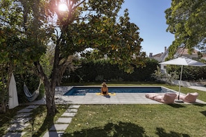 Un giardino sul retro con piscina, amaca e zona patio con cuscini.