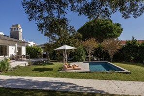 A poolside area with a lounge chair, umbrella, and a hammock. - Casa dos Limões – Oeste: Family Home Between Countryside and Sea (Bombarral)