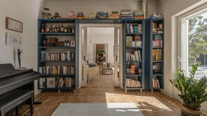 A room with a piano, bookshelves, a plant, and a view through an open door. - Casa dos Limões - Oeste (Bombarral)