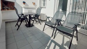 A patio with a table and chairs, a white building with a tiled roof, and a window with metal bars. - Apartment with terrace close to the sea (L'Escala)