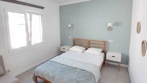 A bedroom with a bed, bedside tables, a nightstand, a chair, and a window. - Apartment with terrace close to the sea (L'Escala)
