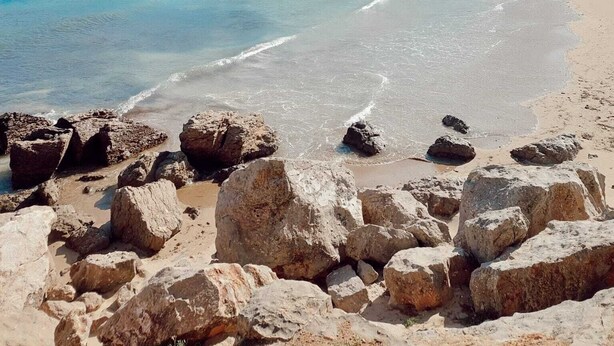 A beach with clear blue water, rocky foreground, and forested hills in the background. - Apartment with terrace close to the sea (L'Escala)