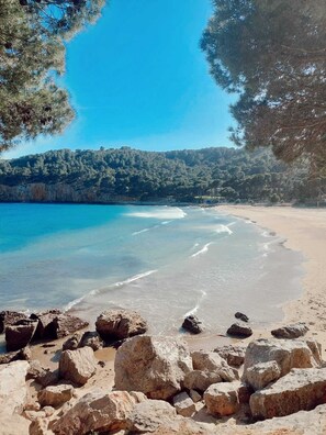 A beach with clear blue water, rocky foreground, and forested hills in the background. - Apartment with a terrace near the ocean (L'Escala)