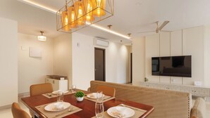 Un'area pranzo moderna con un tavolo in legno apparecchiato per quattro persone, un divano e una TV fissata alla parete.