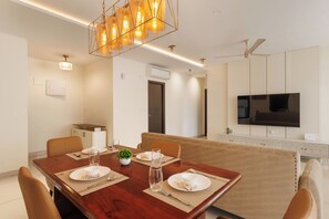 Un espace repas moderne avec une table en bois dressée pour quatre personnes, un canapé et un téléviseur fixé au mur.