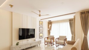 Un soggiorno moderno con una TV a schermo piatto, un divano, due poltrone, una consolle decorativa e una ventola a soffitto.