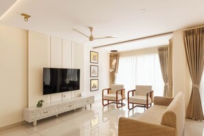 Un salon moderne doté d’un téléviseur à écran plat, d’un canapé, de deux fauteuils, d’une console décorative et d’un ventilateur de plafond.