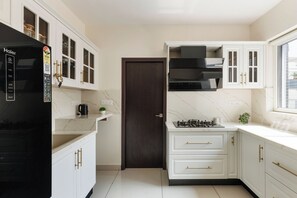 Une cuisine moderne avec des meubles blancs, un réfrigérateur noir et une fenêtre qui laisse entrer la lumière naturelle.