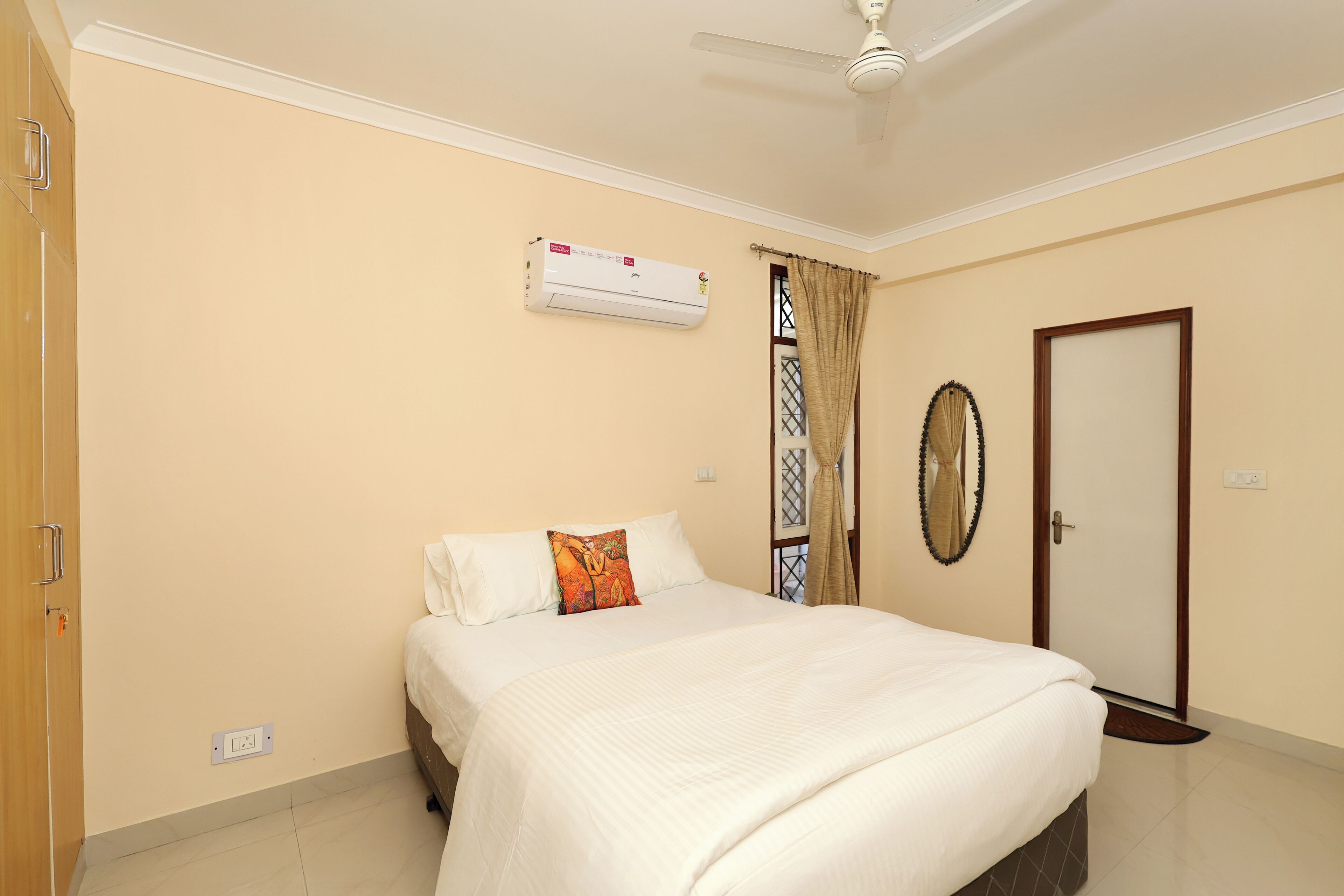 A bedroom with a bed, an air conditioning unit, a door, and a window with curtains.