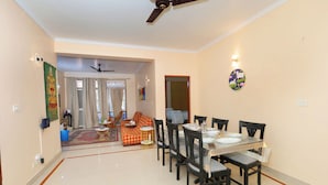 A dining area with a table set for four, surrounded by chairs, in a room with a ceiling fan and a light fixture on the wall. - Taj Luxuria by Red Olive10min to Taj Mahal3bhk (Agra)