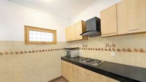 A kitchen with wooden cabinets, a black countertop, a microwave, and a gas stove. - Amber Crest by Redolive10min ~airportdelhi2bhk (New Delhi)