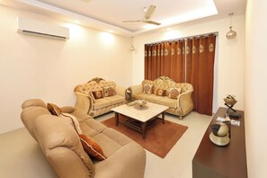 A living room with two sofas, a coffee table, and a small table with decorative items. - Golden Oak by Redolivenr. DLF Golf Course3bhk (Gurugram)