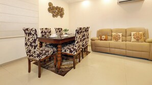 Un coin repas avec une table ronde et des chaises à motifs floraux, un canapé beige agrémenté de coussins à motifs, et un élément décoratif mural.