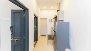 A narrow hallway with a dark blue door on the left, a white door in the center, and a kitchen area with a refrigerator on the right. - Calcutta Heritage by Jadecaps Shyambazar 2BK (Kolkata)