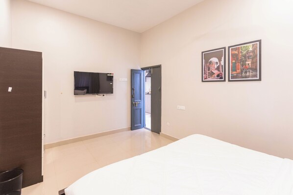 Habitación de hotel con cama, televisor, puerta y dos cuadros en la pared.