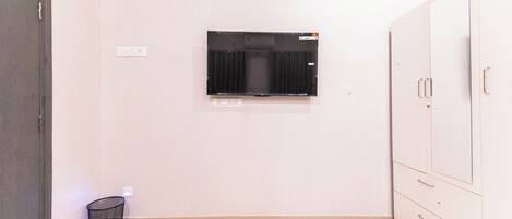 A room with a flat-screen TV mounted on the wall, a trash bin, and a wardrobe with multiple doors.