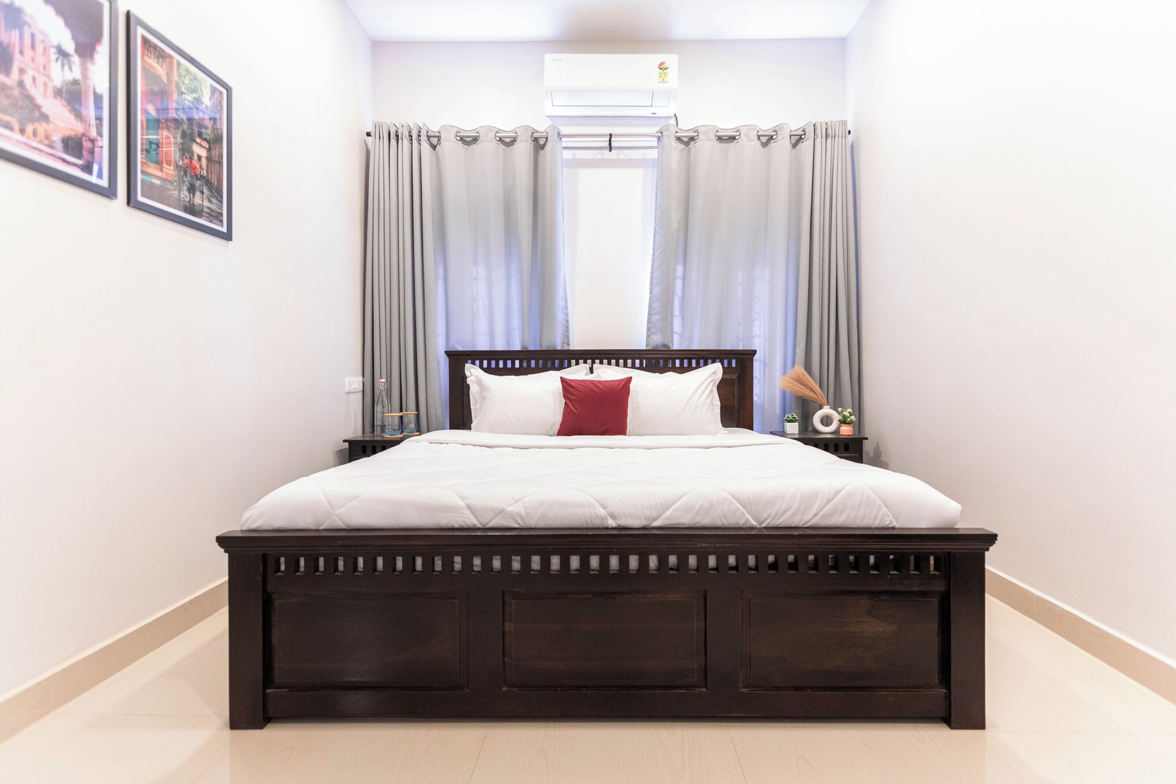 A bedroom with a wooden bed, white bedding, a red pillow, and a nightstand with a lamp.