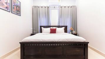 A bedroom with a wooden bed, white bedding, a red pillow, and a nightstand with a lamp.