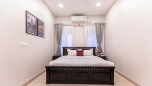 A bedroom with a large bed, a ceiling fan, an air conditioning unit, and two framed pictures on the wall. - Calcutta Heritage by Jadecaps Shyambazar 2BK (Kolkata)