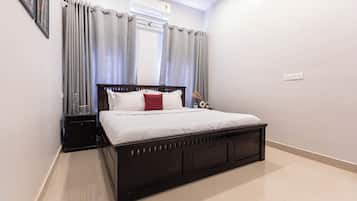 Un dormitorio con una cama de madera oscura, ropa de cama blanca, cortinas grises y una mesita de noche con una lámpara.
