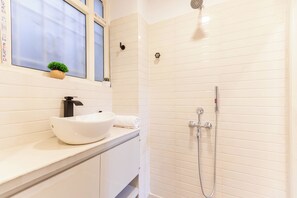 A bathroom with a white sink, a small potted plant, a towel, and a shower with a handheld showerhead. - Calcutta Heritage by Jadecaps Shyambazar 2BK (Kolkata)
