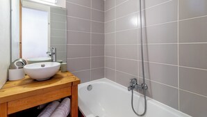 Un bagno con un mobiletto vanità in legno, un lavandino bianco, uno specchio e una vasca da bagno con doccetta.